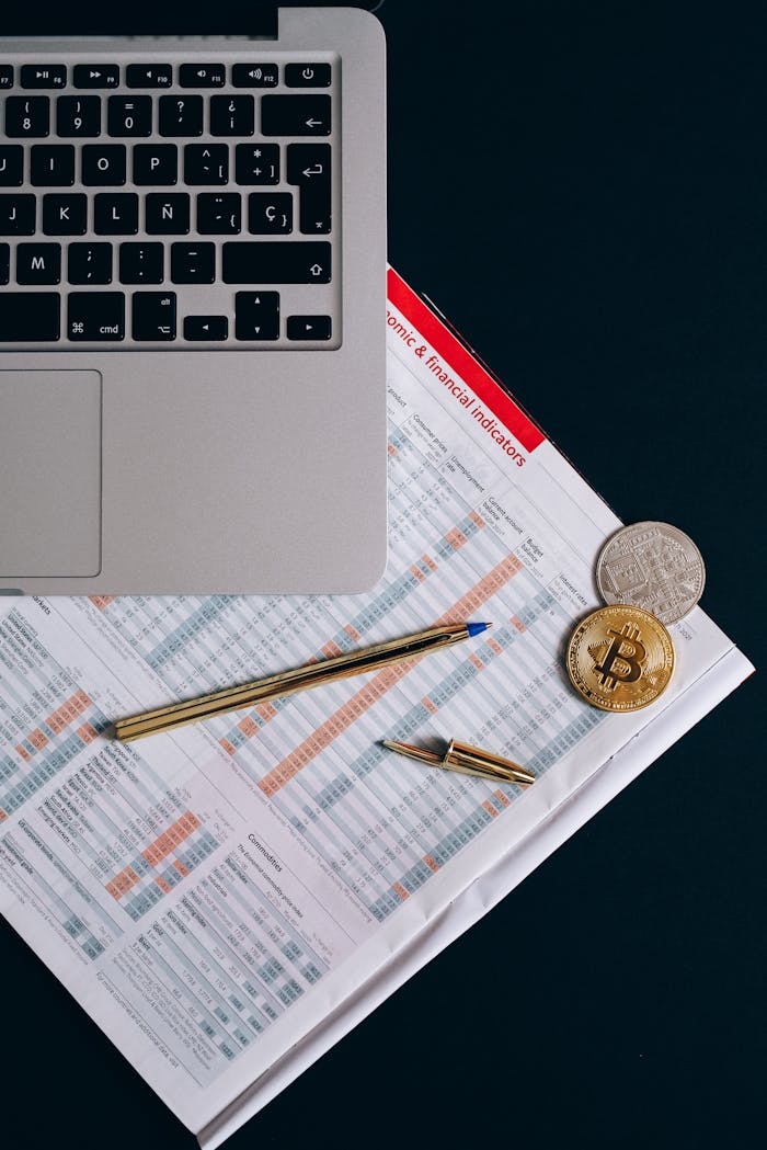 Top view of financial documents, laptop, and cryptocurrency coins on a desk.